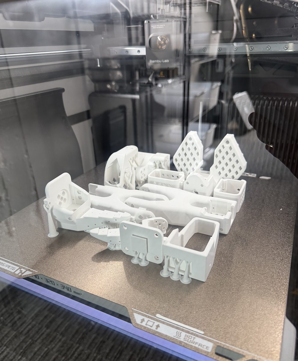 White SO-101 parts on the print bed inside a 3D printer