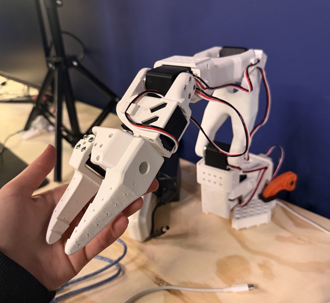 Holding the gripper of the assembled white SO-101 arm, servo wires running along it