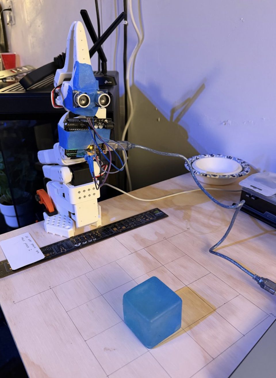 HC-SR04 sensor taped with blue tape to the arm's gripper, above the grid drawn on the desk with a blue block on it